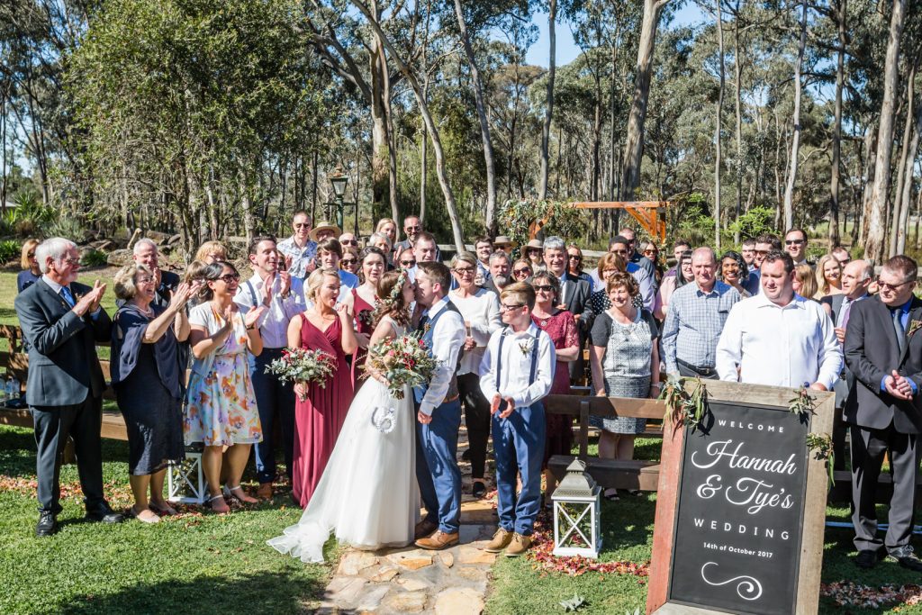 Bride and groom kissing with their guests cheering at the breutiful Gunyah Valley wedding.