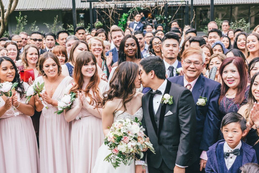 Bride and groom kissing in front of their guests in group photo after ceremony at Poets Lane wedding.