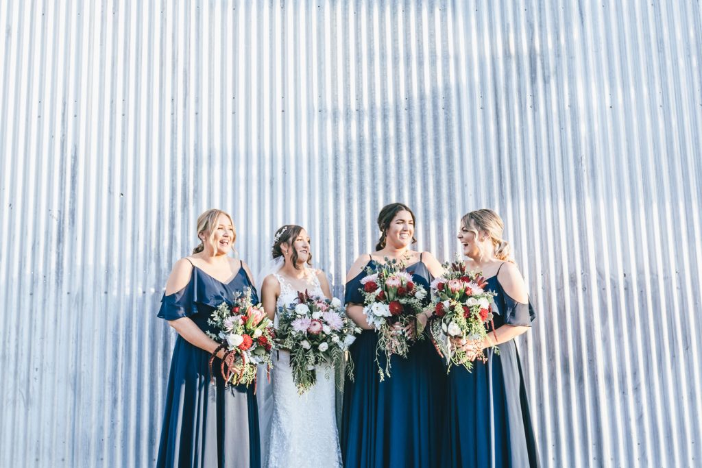 Bride and her bridesmaids posing in front of corrugated wall cladding for Norton Estate wedding.