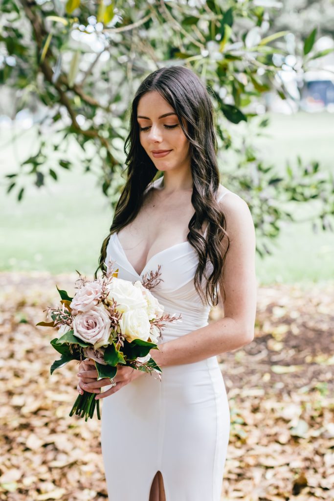 Bride in her simple elegant wedding dress holding bouquet of flowers.