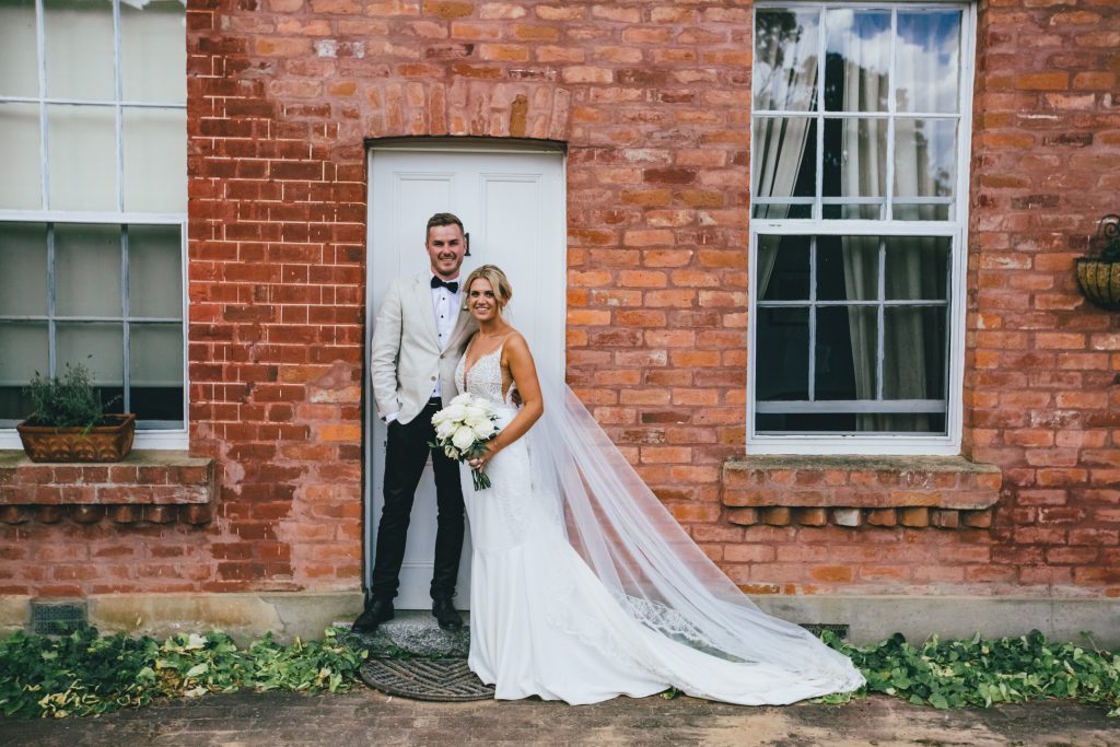 Bride and groom posing in front of brick wall at Ravenswood Homestead Wedding.