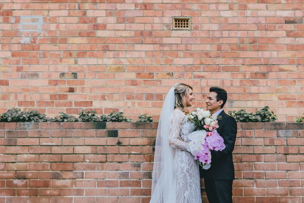 Bride and groom posing in fron t of tall brick wall.