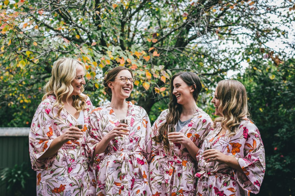 Bride and bridesmaids in floral robes during getting ready while holding champagne glasses.