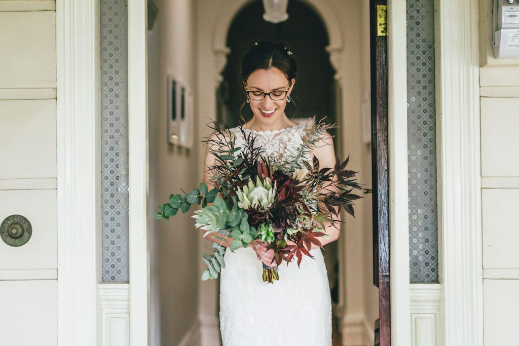 Bride holding her native bouquet of flowers in front on her house door after getting ready.