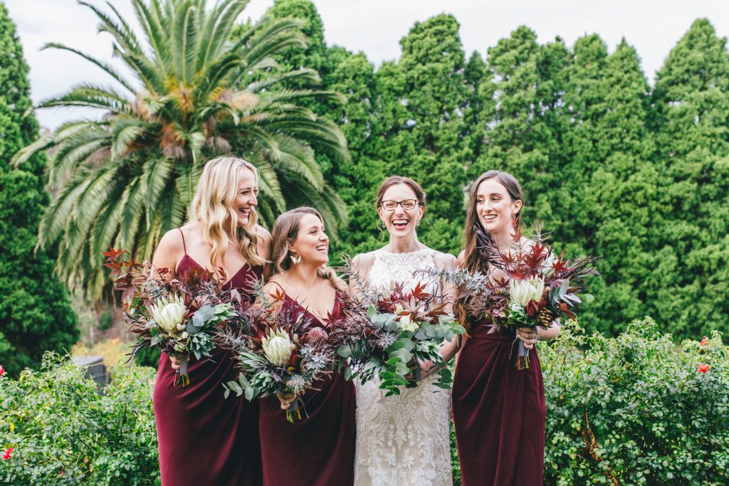 Bride and her bridesmaids in maroon dresses laughing for Farm Vigano South Morang wedding.