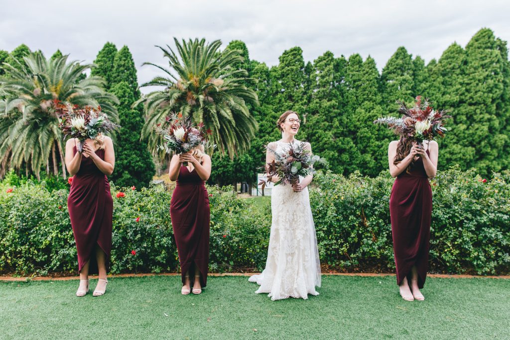 Bride with her bridesmaids hiding their face behind bouquet of flowers for Farm Vigano South Morang wedding.