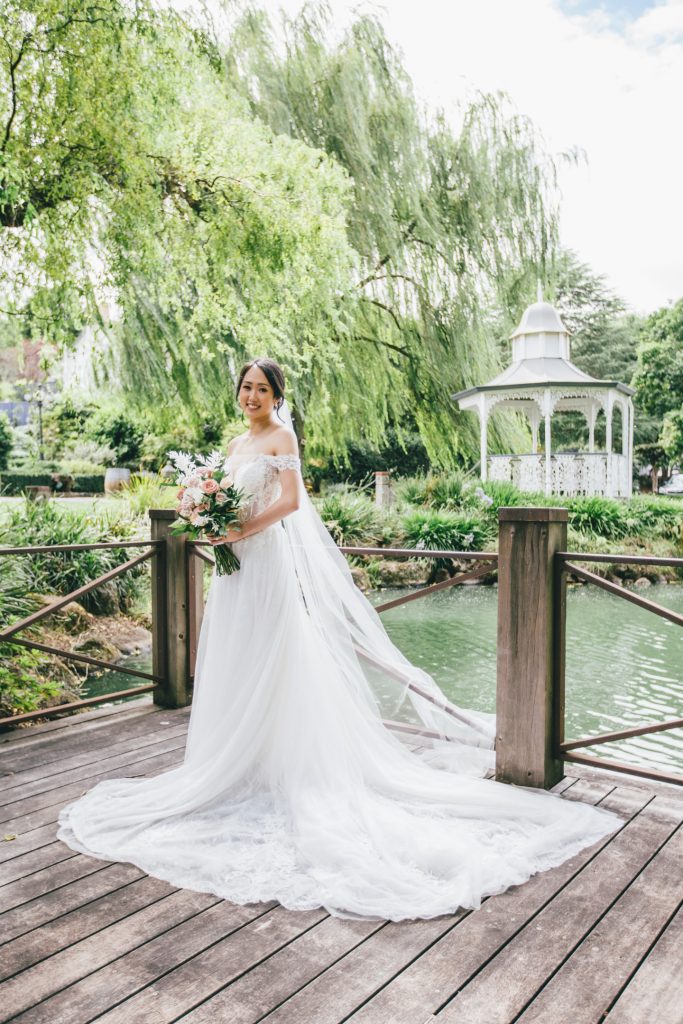 Bride posing in front of lush green garden and pond.