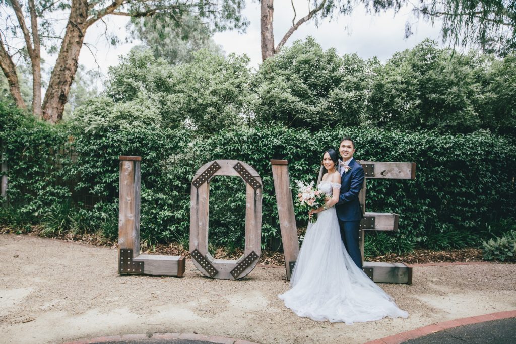 Bride and groom standing in front of big love sign at Ballara Receptions Eltham wedding.