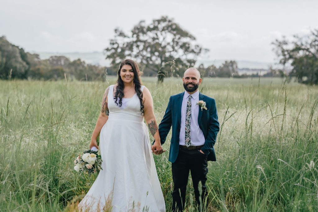Bride and groom holding hands in between tall grasses at Rocklea Farm Stonehaven.
