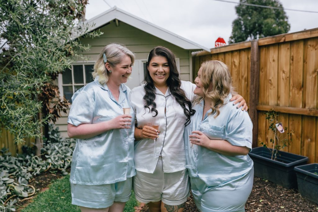 Bride and her bridesmaids wearing bridal silk pyjamas while holding champagne glass.