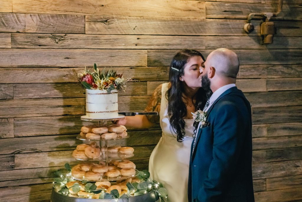 Bride and groom cutting rustic wedding cake with donut tower.