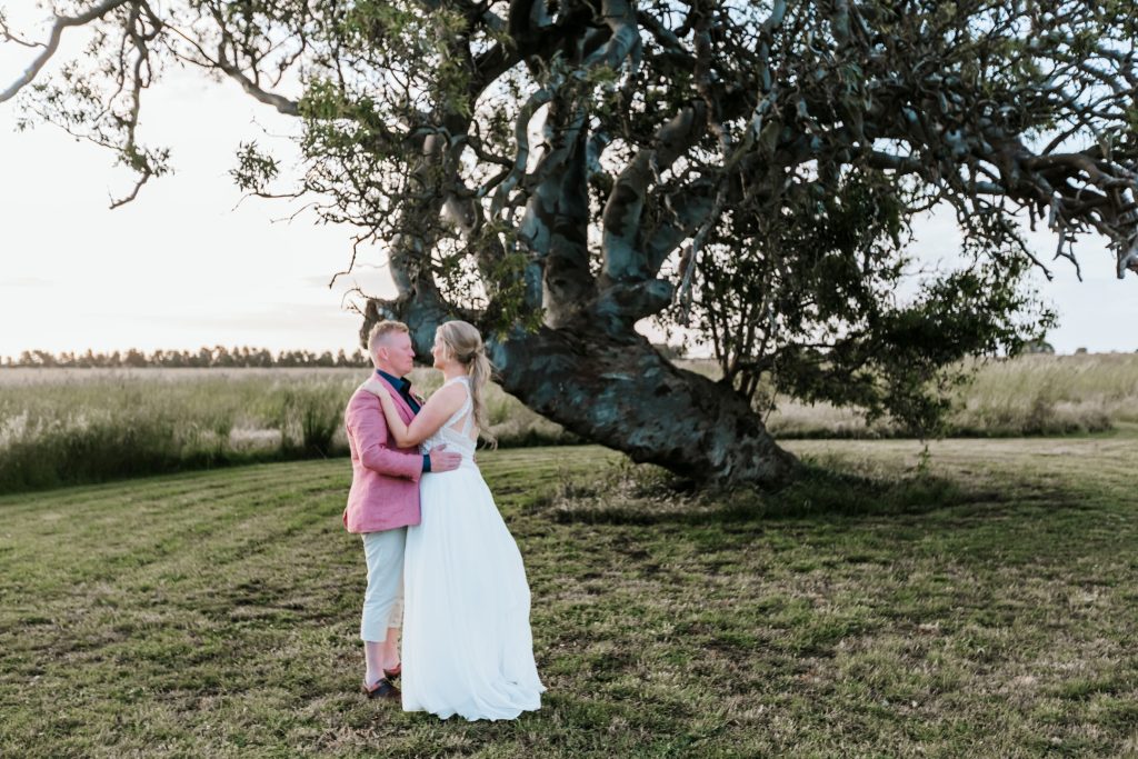 Bride and groom embracing in front of beautiful big tree for Rocklea Farm wedding.