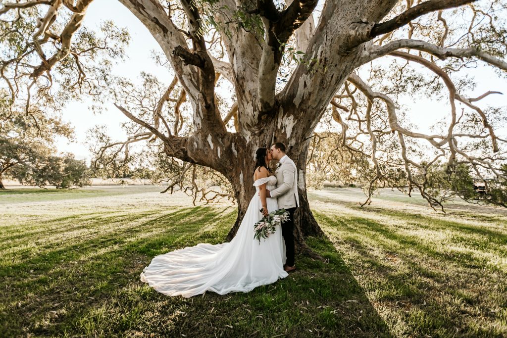 bride and groom holding each other under an oak tree at Rocklea Farm. This photo is captured by WIDFOTOGRAFIA Melbourne Wedding Photographer
