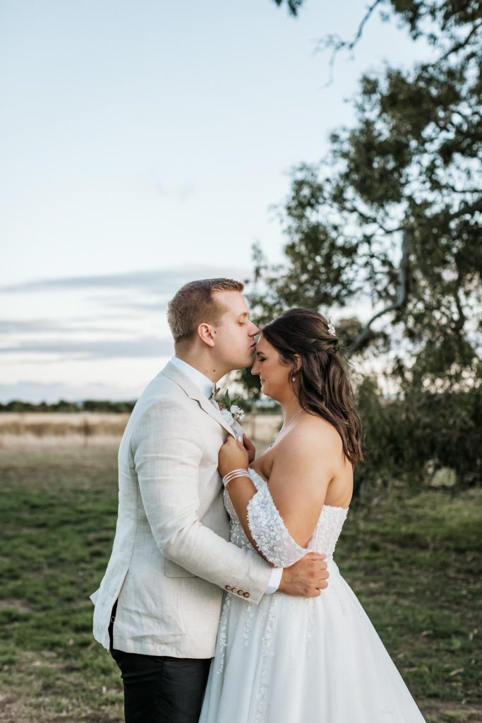 Groom kissing his bride forehead while embracing for Rocklea Farm Stonehaven wedding.