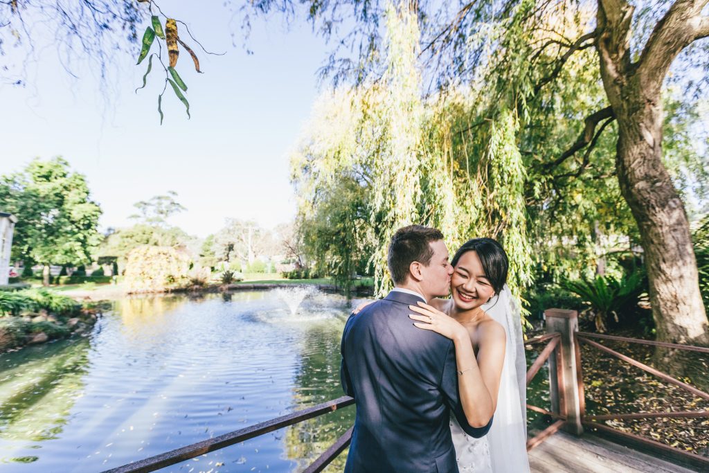 Groom kissing his bride in front of the garden pond at Ballara Receptions Eltham.