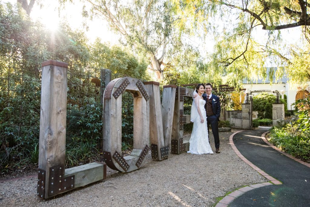 Bride and groom in front of big wooden love signs at Ballara Receptions Eltham.